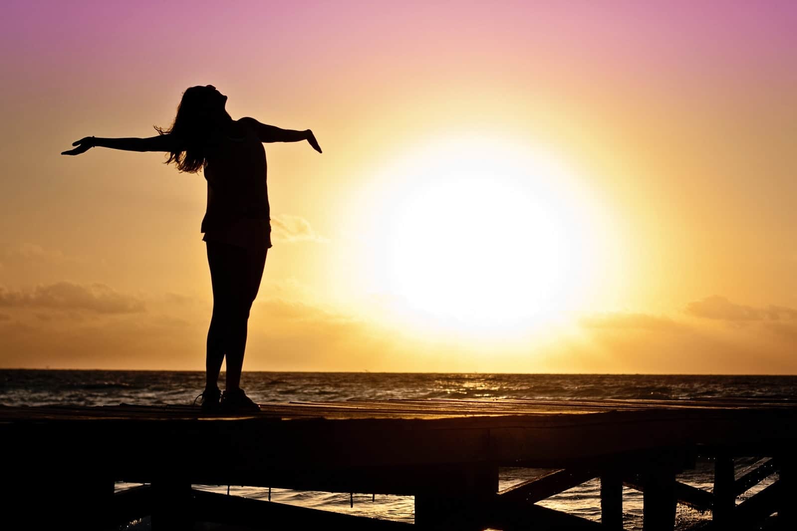 a woman standing arms outstretched toward the sunset symbolizing freedom from energy vampires